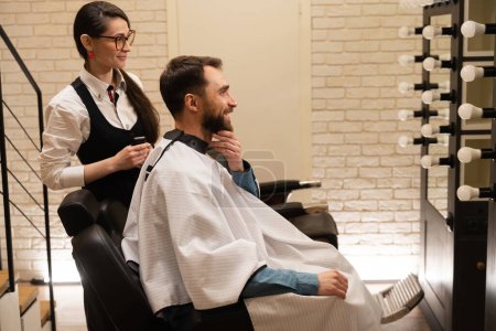 Foto de Hombre en una barbería se comunica con un maestro, una mujer tiene un cortador en sus manos - Imagen libre de derechos