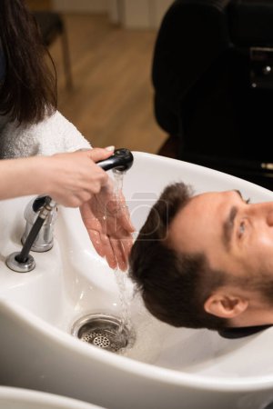 Photo for Female washes the head of a client at a special sink, male in a protective cape - Royalty Free Image