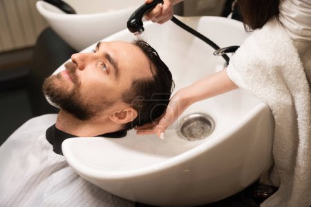 Téléchargez les photos : Client aime la procédure de lavage des cheveux dans le salon de coiffure, l'artisan utilise un évier spécial - en image libre de droit