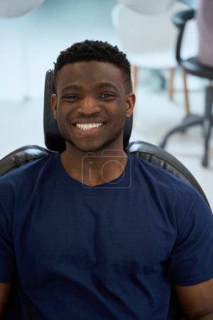 Photo for Handsome African American man stomatology client sitting in comfortable dental chair and looking at camera with healthy toothy smile - Royalty Free Image