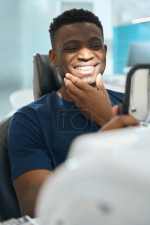Photo for Happy African American man looking at his healthy teeth and smiling, satisfied with qualified stomatological team work, private clinic service - Royalty Free Image