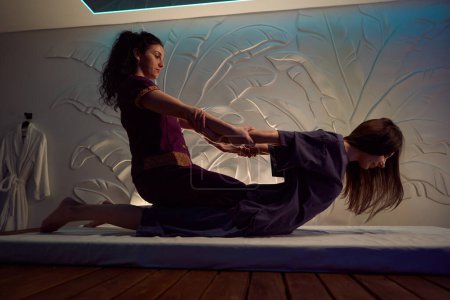 Foto de Vista lateral del masajista enfocado tirando del torso femenino del cliente hacia arriba fuera del futón durante la sesión de masaje tailandés - Imagen libre de derechos