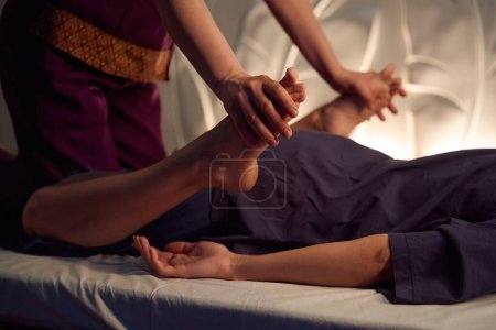 Foto de Foto recortada de una paciente femenina acostada propensa al futón mientras masoterapeuta presiona sus pies hacia las nalgas - Imagen libre de derechos