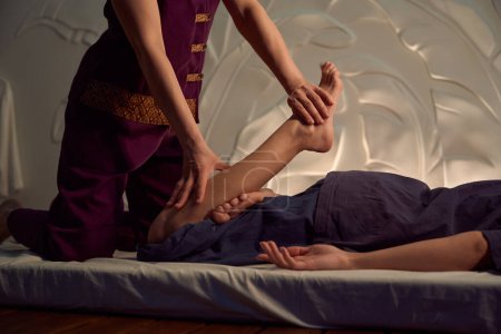Téléchargez les photos : Photo recadrée de masseuse poussant client jambe courbée avec les deux mains vers la région fessière - en image libre de droit