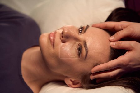Photo for Closeup of tranquil young patient lying supine while massotherapist massaging her head - Royalty Free Image