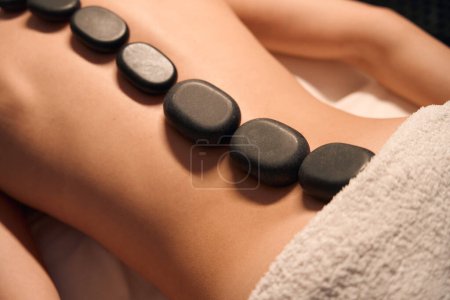 Photo for Closeup of naked woman lying prone with hot flat black stones positioned along spine - Royalty Free Image