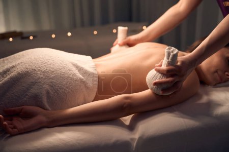 Photo for Young woman lying prone while massotherapist massaging her arms with pair of herbal bags - Royalty Free Image