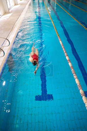 Téléchargez les photos : Vue du dessus de la nageuse en bonnet de bain et maillot de bain nageant sur le dos dans l'eau - en image libre de droit