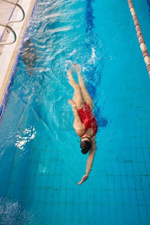 Photo for Top view of sportswoman in goggles and swim cap practicing backstroke in water - Royalty Free Image