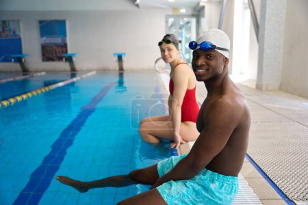 Foto de Deportista sonriente y deportista satisfecho sentado en el borde de la piscina cubierta - Imagen libre de derechos