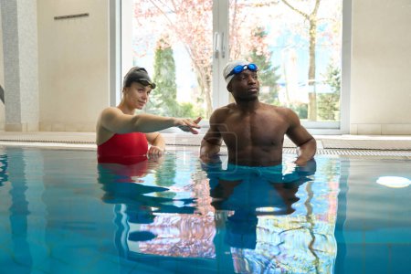 Foto de Entrenador de natación señalando algo a su estudiante en la piscina durante el entrenamiento acuático - Imagen libre de derechos