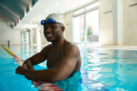 Téléchargez les photos : Joyeux jeune nageur afro-américain penché sur le diviseur de voie dans l'eau turquoise - en image libre de droit