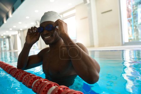 Téléchargez les photos : Athlète souriant debout devant le séparateur de voie de piscine et portant des lunettes de cyan - en image libre de droit