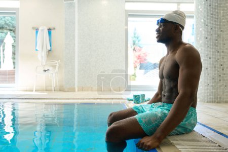 Téléchargez les photos : Vue latérale du sportif joyeux assis sur le bord de la piscine intérieure - en image libre de droit
