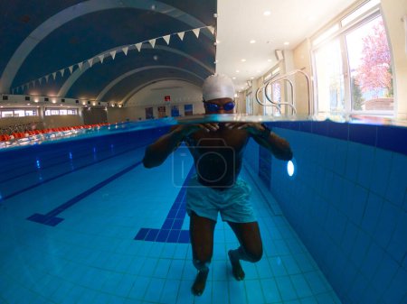 Téléchargez les photos : Nageur afro-américain adulte en bonnet de bain et lunettes immergées sous l'eau - en image libre de droit