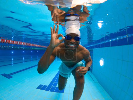 Photo for Cheerful athlete in swimming cap and goggles making OK hand sign under water - Royalty Free Image