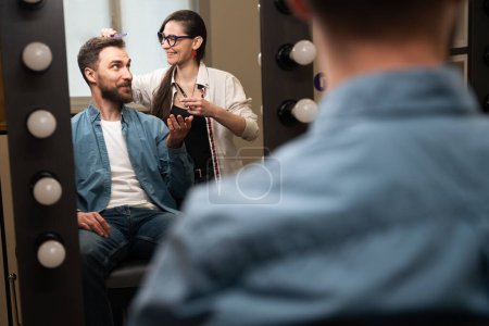 Foto de Maestro peluquero en el lugar de trabajo se comunica con el cliente, el hombre se encuentra en la silla de peluquería delante del espejo - Imagen libre de derechos