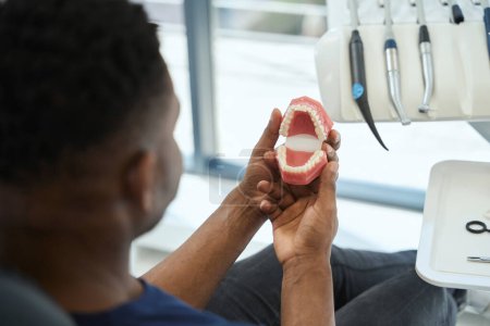 Téléchargez les photos : Client masculin de la clinique de stomatologie esthétique regardant le modèle 3D de sa mâchoire, bon exemple de redressement des dents après le port d'appareils orthopédiques - en image libre de droit