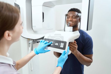 Téléchargez les photos : Homme debout dans la clinique près de l'appareil de tomographie informatique. Image tomographique du crâne et des dents - en image libre de droit