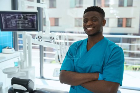 Téléchargez les photos : Homme souriant en costume bleu debout près du patient dans le bureau de dentisterie, regardant la caméra - en image libre de droit