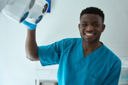 Foto de Joven con traje azul instala equipo antes de trabajar en el hospital, mirando a la cámara - Imagen libre de derechos
