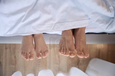 Foto de Acercamiento de dos pares de pies mirando desde debajo de una manta blanca - Imagen libre de derechos