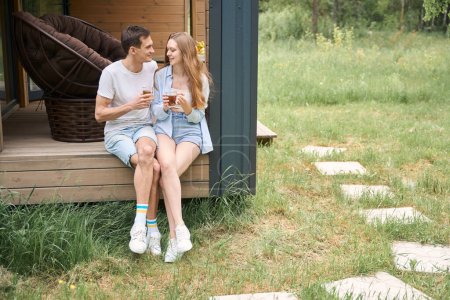 Téléchargez les photos : Couple heureux parlant tout en buvant du thé et assis sur le bord de la terrasse - en image libre de droit