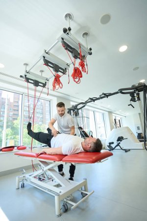 Photo for Client doing supine bridging with rotation on suspension trainer with help of fitness instructor - Royalty Free Image