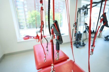 Téléchargez les photos : Entraîneur de suspension avec sangles rouges et élingues parmi d'autres appareils de fitness dans la salle d'exercice - en image libre de droit