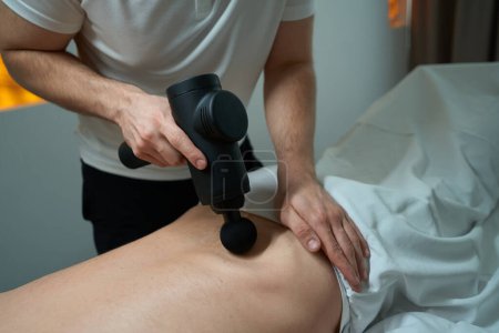 Photo for Cropped photo of physiotherapist loosening tight muscles in patient lumbar region with handheld massage gun - Royalty Free Image