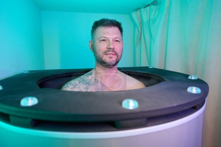 Portrait of calm Caucasian middle-aged man sitting in cryobarrel in wellness center
