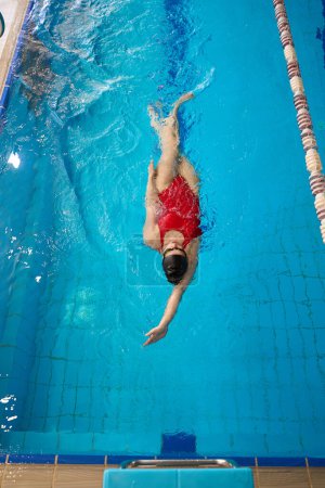 Téléchargez les photos : Vue du dessus de l'athlète féminine en maillot de bain et bonnet de bain effectuant le dos dans la piscine - en image libre de droit