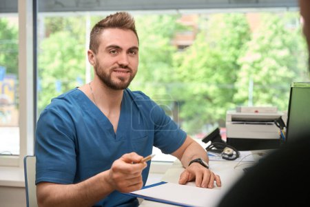 Foto de Trabajador sanitario con lápiz en la mano y portapapeles sentado en el escritorio hablando con la persona - Imagen libre de derechos