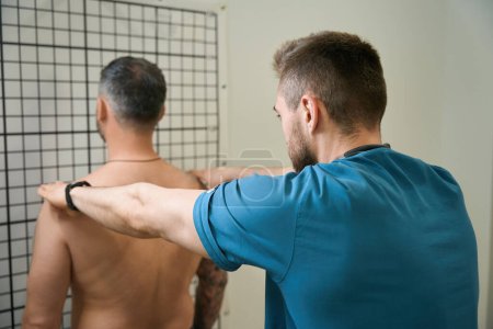 Experienced physical therapist palpating trapezius muscle in adult male patient upper back