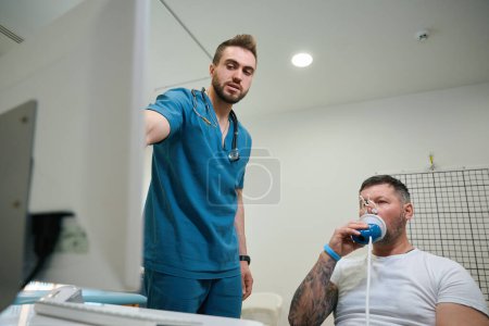 Téléchargez les photos : Patient avec clip nasal respirant dans l'embout buccal du spiromètre tandis que le médecin surveille ses lectures de spirogrammes sur l'écran de l'ordinateur - en image libre de droit