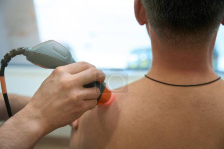 Photo for Closeup of doctor hand directing laser beam at upper trapezius trigger point in adult person - Royalty Free Image