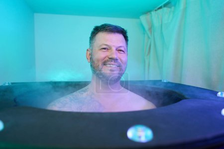 Photo for Portrait of joyful adult male sitting in cryobarrel cabin in wellness center - Royalty Free Image
