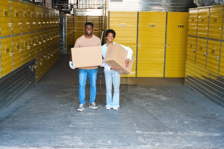 Téléchargez les photos : Un jeune couple afro-américain loue une unité de stockage, les gars ont des boîtes en carton dans leurs mains - en image libre de droit