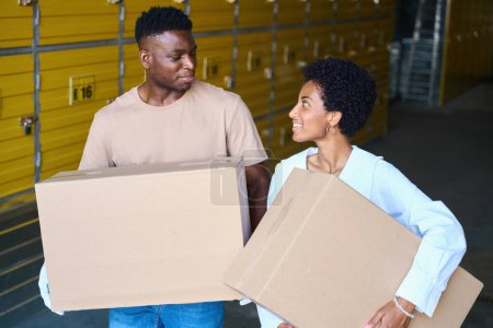 Téléchargez les photos : Mignons afro-américains dans des vêtements décontractés stand dans un entrepôt avec des boîtes en carton dans leurs mains - en image libre de droit
