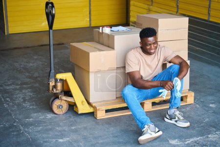 Photo for Young man sat down to rest on cargo cart, on the cart there were cardboard boxes and a tape dispenser - Royalty Free Image