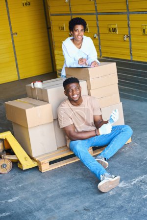 Téléchargez les photos : Employés de l'entrepôt, une femme gestionnaire et une chargeuse, sur le lieu de travail près d'un chariot à cargaison avec boîtes en carton - en image libre de droit
