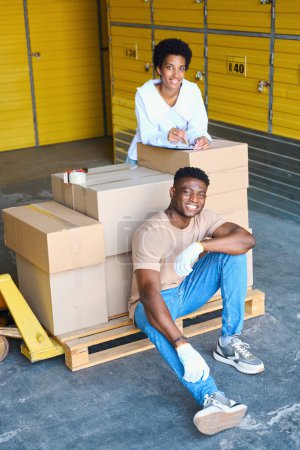 Téléchargez les photos : Employés de l'entrepôt, gérant et chargeur, sur le lieu de travail près d'un chariot à cargaison avec boîtes en carton - en image libre de droit