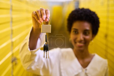 Photo for African American woman with neat manicure holds a padlock with keys, she is in a warehouse - Royalty Free Image