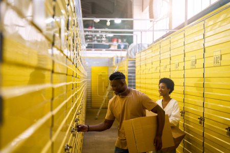 Photo for African American guy opens a storage unit, next to his girlfriend with cardboard boxes - Royalty Free Image