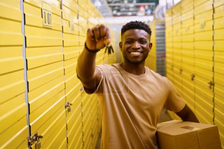 Photo for African American man stands with keys and a box near storage containers, the cells are numbered - Royalty Free Image