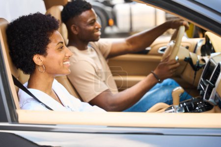 Téléchargez les photos : Heureux couple afro-américain voyageant dans une voiture confortable, homme conduisant la voiture - en image libre de droit