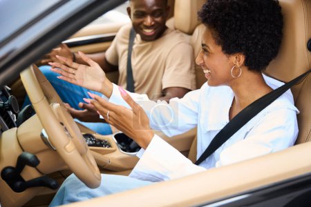 Téléchargez les photos : Deux jeunes Afro-Américains, homme et femme, sont assis dans une voiture moderne, les gars s'amusent à parler - en image libre de droit