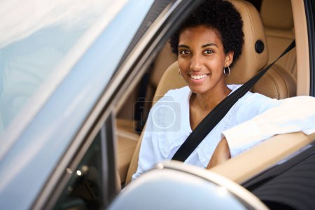 Téléchargez les photos : Jeune femme afro-américaine souriante dans une voiture confortable, dans un intérieur de voiture design élégant - en image libre de droit