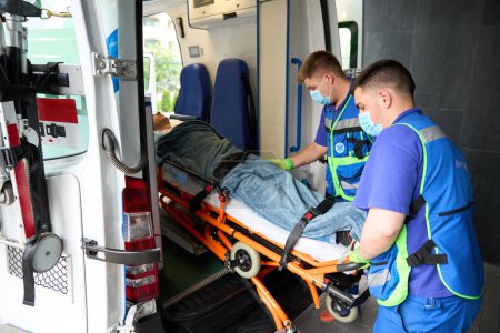 Foto de Paramédicos jóvenes descargan a un paciente de una ambulancia, el paciente se fija en una camilla especial - Imagen libre de derechos
