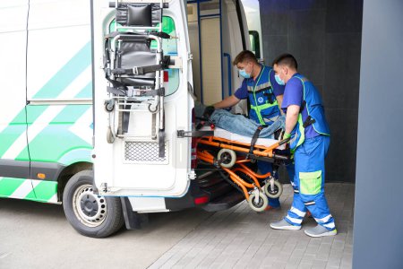 Téléchargez les photos : Les ambulanciers déchargent la victime dans un accident d'ambulance, le patient est fixé sur une civière spéciale - en image libre de droit